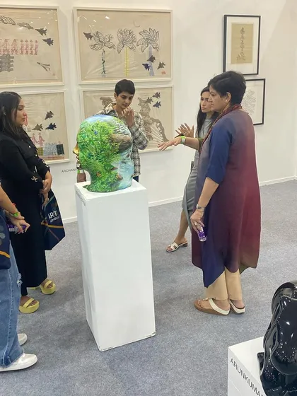 A gallerist explaining Venkat Bothsa's sculpture to a group of young visitors.