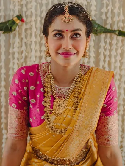 A bride in a yellow and pink Kanchipuram saree. Her custom pink blouse features delicate butti embroidery, perfect for a pre-wedding pooja.
