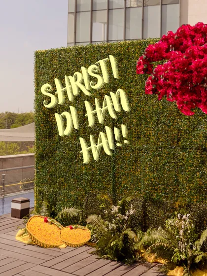 A fun and personalized photo wall for the Haldi ceremony, featuring the phrase "Shristi Di Han Hai!!" on a lush green backdrop.