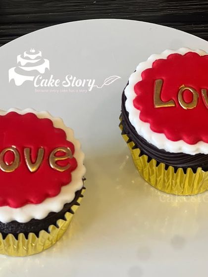 A pair of classic "Love" cupcakes. The combination of rich chocolate cake, white frosting, and red fondant with golden letters is perfect for Valentine's or an anniversary.