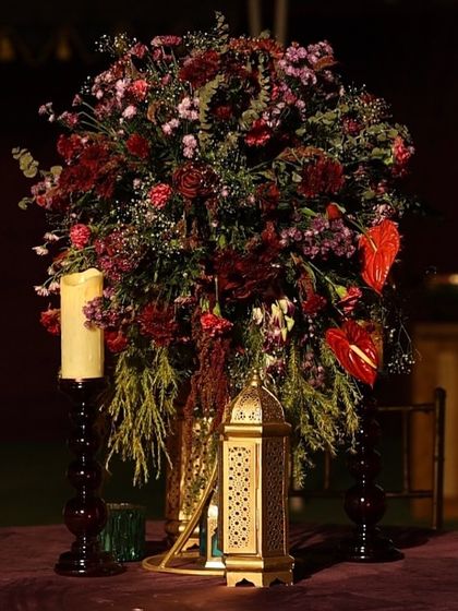 A detailed shot of a floral centerpiece, featuring red anthuriums and carnations, paired with a golden Moroccan lantern and tall candles.