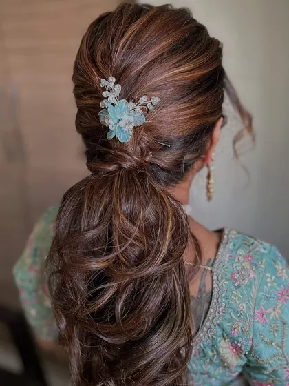 A voluminous ponytail with soft curls and a pretty blue floral accessory. This hairstyle is perfect for a reception or cocktail party.
