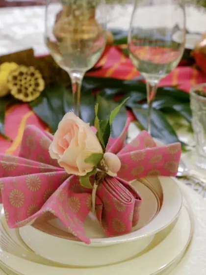 A beautifully folded napkin adds life and class to any tablescape. This fan-shaped fold, secured with a floral accent, brings a touch of elegance and color to the place setting.