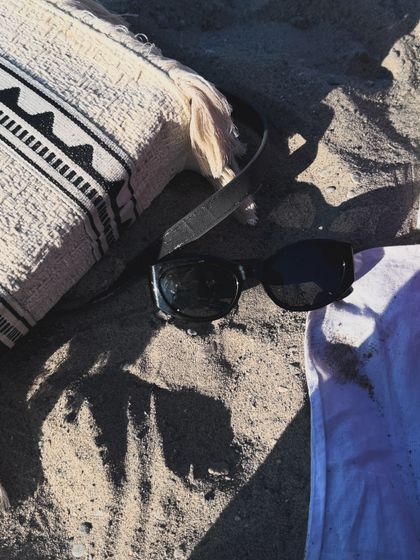 An aesthetic detail shot of sunglasses and a bag on the sand.
