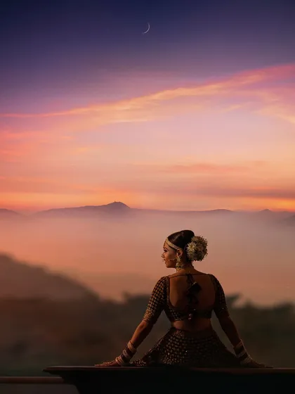 A moment of serene reflection. A bride, adorned in traditional attire, looks out at a breathtaking sunset over the mountains. We seek out these opportunities for quiet, beautiful portraits amidst the celebration.