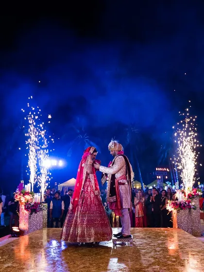 A dramatic varmala moment at a beach wedding, with the couple framed by pyrotechnics against the night sky. This showcases our ability to create spectacular moments in any setting.