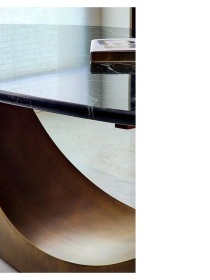 The base of a bespoke table, where a curved, sculptural form in aged brass supports a black marble top. We design and produce many custom objects to ensure every piece contributes to the home's narrative.