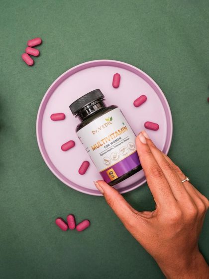 A top-down flat lay of Dr. Vedic Multivitamin for Women. The capsules are arranged like a clock around a pink plate, creating a playful and visually interesting composition.