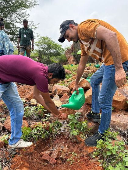 Two volunteers from Beumer Group work together to water a newly planted sapling on the rocky slopes of Aravali Nagar Van, braving the heat to make a difference.