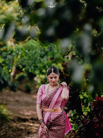 A portrait of a bride in a pink saree, walking through a lush green path, capturing her grace from behind.