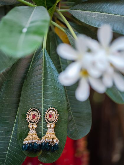 A pair of beautiful jhumka earrings with ruby and emerald details, artistically placed on a green leaf. This shot highlights the elegance of the bridal jewelry against a natural backdrop.