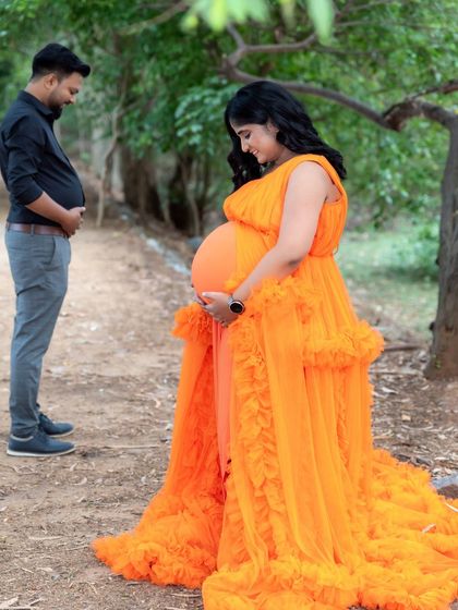 A playful and sweet photo of an expecting couple. The mom-to-be looks down at her baby bump while her partner stands behind her, also holding his belly.