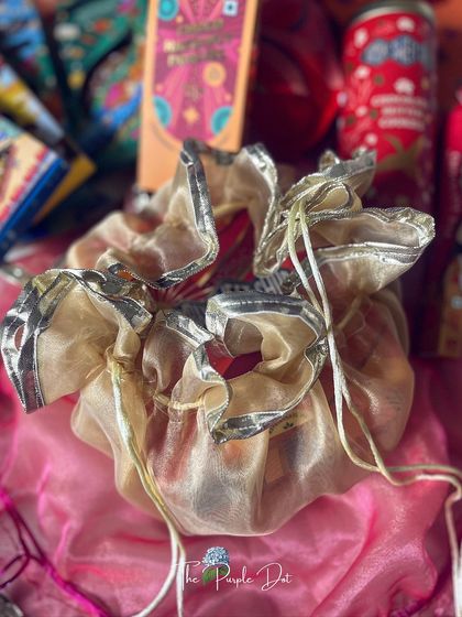 A traditional organza potli with gota work, used to hold small treats or gifts within a larger festive hamper.
