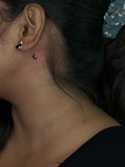 A tiny crescent moon tattoo placed discreetly behind the ear. This is a very popular spot for a first or small tattoo.
