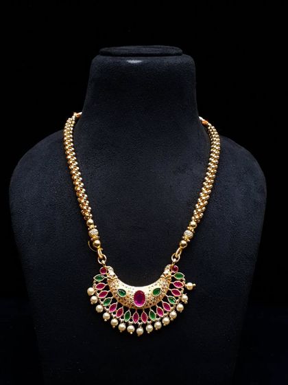 A simple yet elegant necklace with a half-moon pendant studded with ruby and green stones. The gold-beaded chain completes the traditional look.