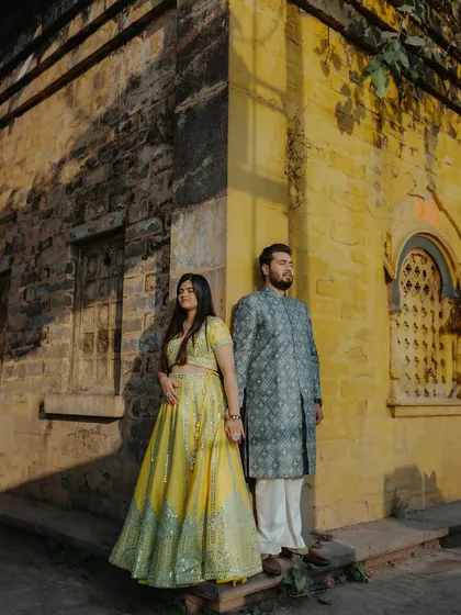 A full-length portrait of the couple standing against a rustic yellow wall, with dramatic shadows from the morning sun.