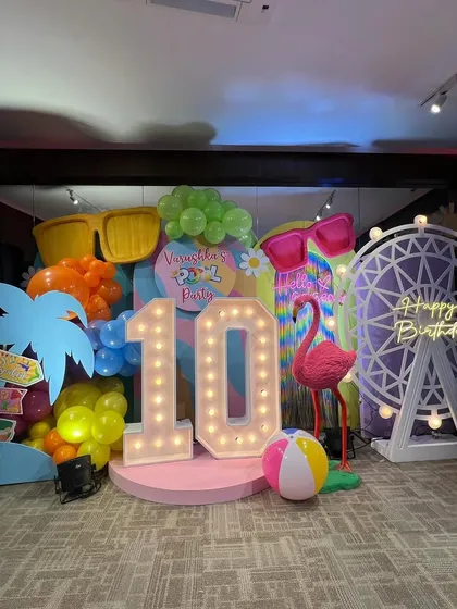 A vibrant pool party setup with a large "10" marquee, giant sunglasses, a flamingo, and a Ferris wheel prop for a fun-filled birthday.