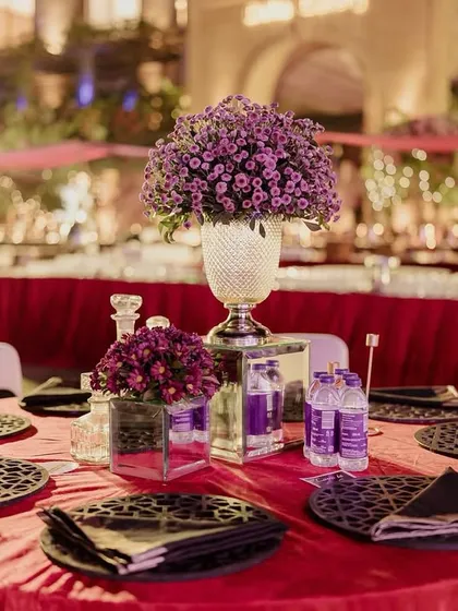 A table setting from the Sangeet, featuring custom-printed placemats, deep purple flowers, and a bold red tablecloth.