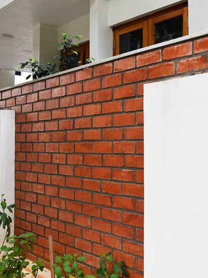 The boundary wall combines clean white plaster with a section of exposed brick, introducing the home's material palette right from the street.