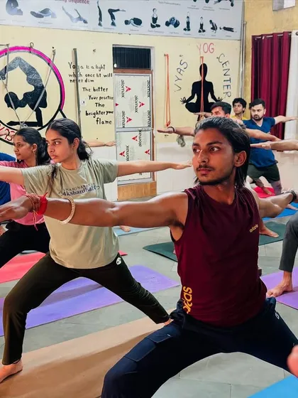 A class of dedicated students practicing Virabhadrasana II (Warrior II). The focus and determination in their eyes show the strength they are building, both physically and mentally.