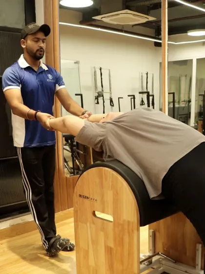 A coach assists a client with a deep backbend over the ladder barrel. This is a fantastic stretch for opening up the chest and improving spinal flexibility with proper support.