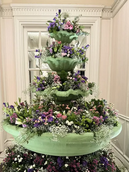 A mint-green fountain overflowing with a cascade of purple and white flowers, serving as a stunning and unique statement piece.