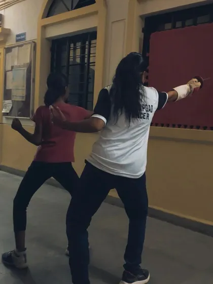 A senior fencer demonstrates correct form to a junior student. Peer learning is an important part of our club's culture, fostering a supportive environment.