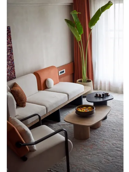 The living room of 'A Den' is filled with earthy tones and natural materials. The custom sofa and coffee tables create a comfortable and inviting seating area.