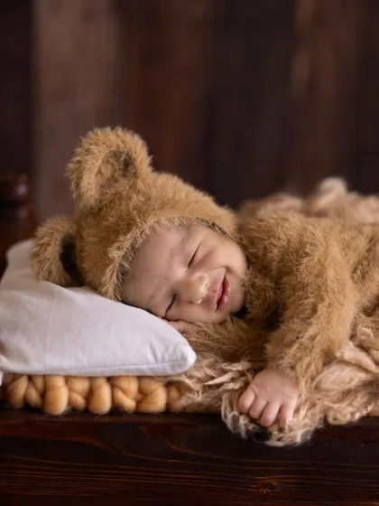 A duplicate of image 29, a close-up of a smiling newborn in a teddy bear outfit.