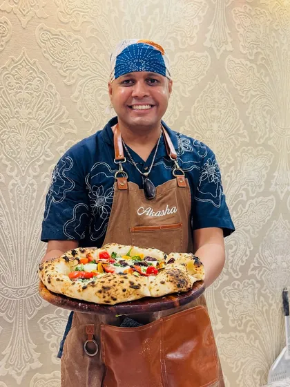 Holding up a freshly made veggie pizza. The crust has a beautiful puffy cornicione and classic leopard spotting from the high-heat oven.