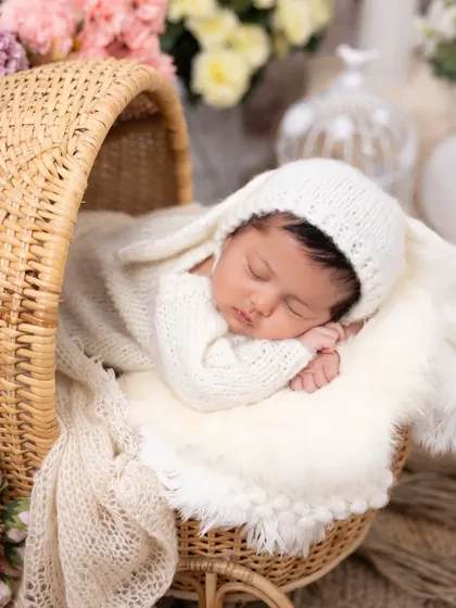 A close-up of our sleeping bunny theme, this time in a charming rattan bassinet. The soft, warm lighting emphasizes the baby's peaceful sleep and the cozy knit texture of the outfit.