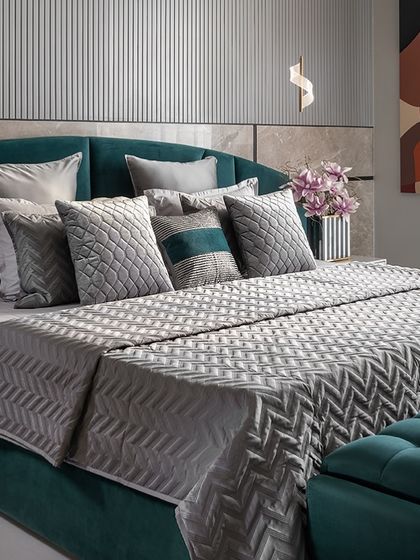 The art of comfort and style is in the soft furnishings. Here, a mix of geometric and solid grey and teal cushions adds depth and sophistication to a bed with a deep teal headboard.