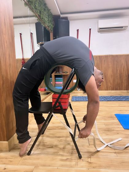 A student works on a deep backbend, using a chair, wheel, and strap for support. This demonstrates how props can be combined to assist in advanced postures safely.