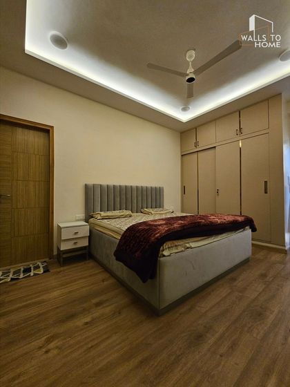 This minimalist bedroom features a grey upholstered bed with a channel-tufted headboard and a sliding wardrobe. The wooden flooring adds warmth to the clean, contemporary design.