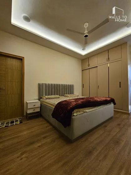 This minimalist bedroom features a grey upholstered bed with a channel-tufted headboard and a sliding wardrobe. The wooden flooring adds warmth to the clean, contemporary design.