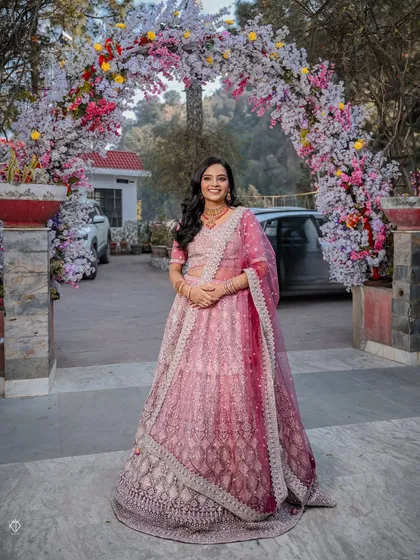 A full-length portrait of the bride standing under a stunning floral arch, showcasing her complete engagement look from head to toe.