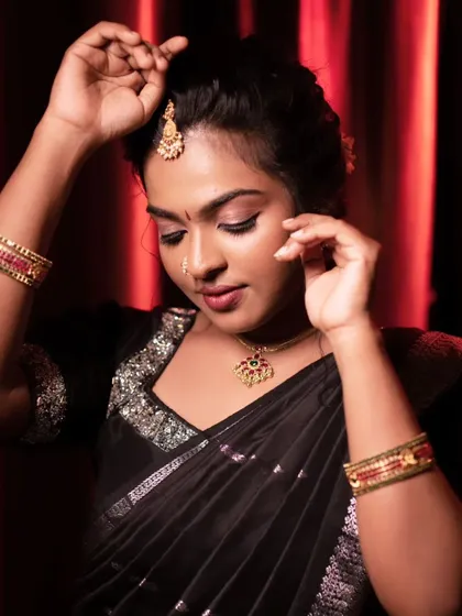 Adjusting the jewelry on this beautiful model. The makeup is bold and defined, perfectly complementing her black saree and gold accessories.