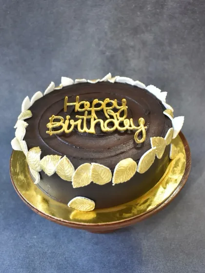 A classic and decadent caramel ganache cake. The rich, glossy chocolate ganache is beautifully contrasted with delicate white and gold leaves, perfect for an elegant birthday.