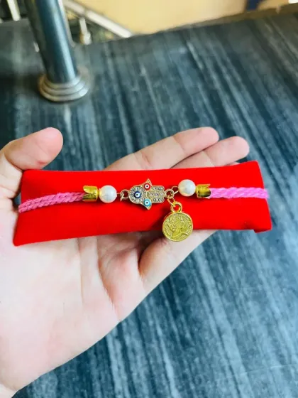 This adjustable band features a Hamsa hand charm for protection, paired with a coin charm on a pink and red thread.