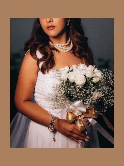 A classic portrait of the bride in her white wedding gown, holding a bouquet of white roses. The warm tones give this image a timeless, romantic feel.