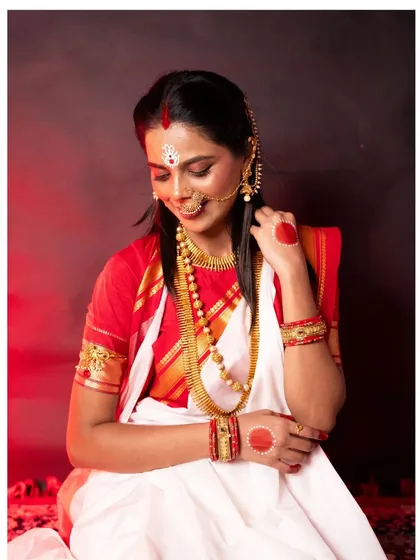 A conceptual portrait from a Durga Puja themed shoot. This image captures the essence of Bengali tradition, with the intricate 'sholar saaj', the classic white and red saree, and a serene, divine expression.
