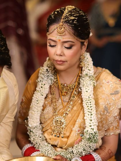 A traditional South Indian bridal updo, featuring a center part and a bun adorned with jasmine flowers. This hairstyle is perfect for accommodating the traditional gold matha patti.