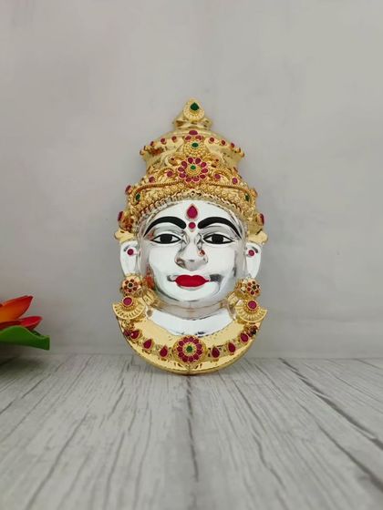 A gold-plated Lakshmi face with red and green stone work. The combination of gold and silver tones gives it a rich and festive look.