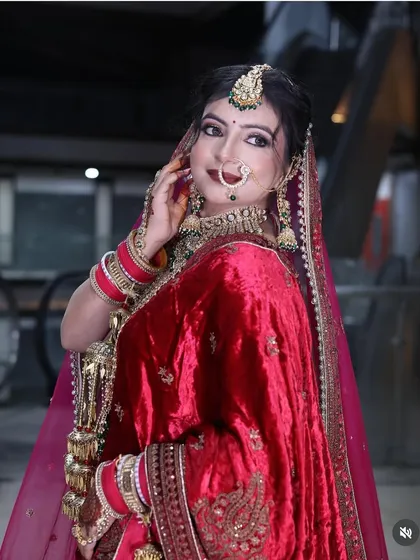 A classic bridal pose in a red velvet lehenga, highlighting the rich texture of the fabric and the intricate gold embroidery.