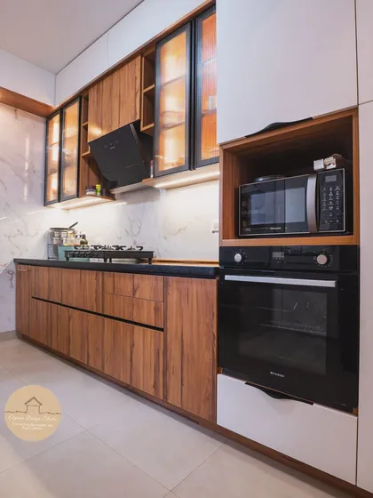 A kitchen should be both beautiful and functional. This contemporary kitchen at a Godrej Air Hoodi project showcases a seamless blend of warm wooden textures and glossy white laminate. The fluted glass cabinets with interior lighting add a touch of sophistication while providing practical storage.