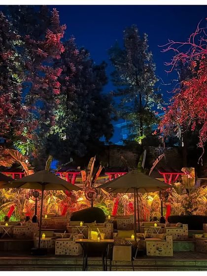 The outdoor seating area of the jungle party, illuminated with dramatic red and yellow lights. The use of color transforms the natural landscape into a surreal, high-energy environment.