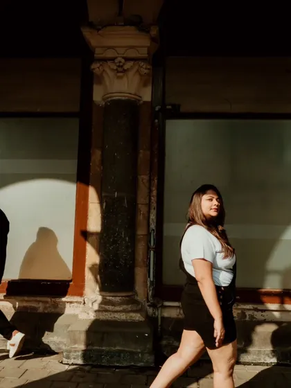 A candid shot of a woman walking through the dramatic shadows of Mumbai's colonial architecture. We love playing with light and shadow to create artistic and moody urban portraits.