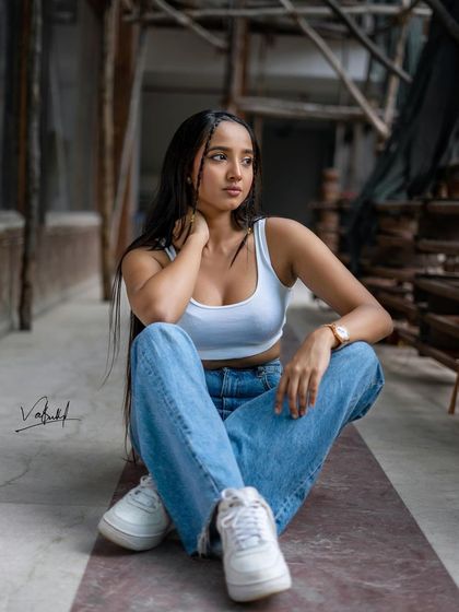 A full-body shot that captures the complete street fashion look, from the casual crop top and denim to the fresh white sneakers. The industrial setting adds a gritty, urban texture to the photo.