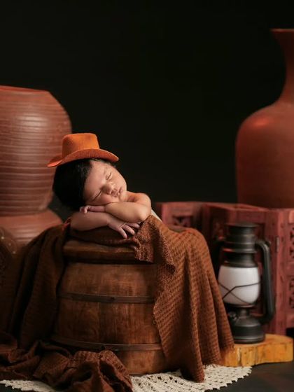 A newborn in a tiny hat sleeps peacefully amidst a collection of terracotta pots and a lantern, creating an earthy and rustic feel.
