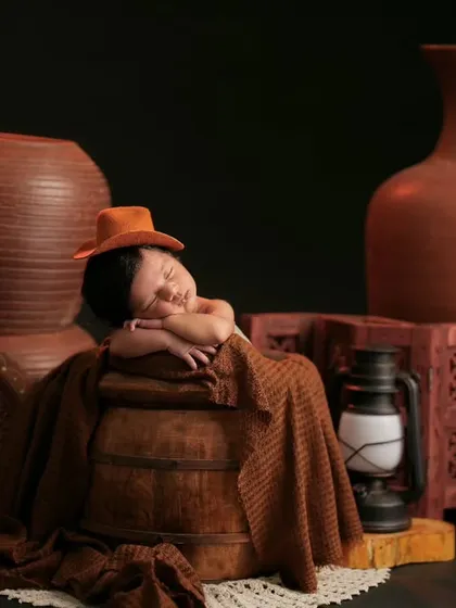 A newborn in a tiny hat sleeps peacefully amidst a collection of terracotta pots and a lantern, creating an earthy and rustic feel.